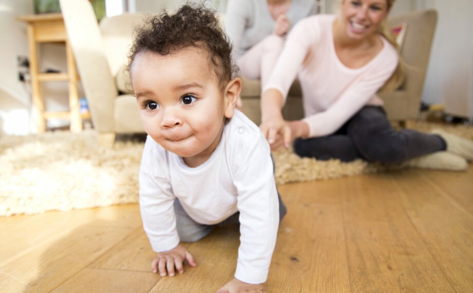 Female couple watch proudly as their baby son crawls along the floor